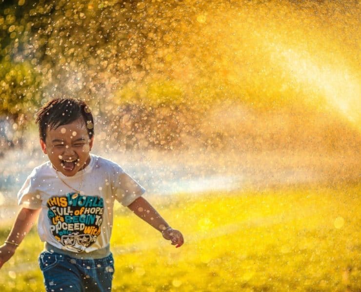 boy running through water sprinkler
