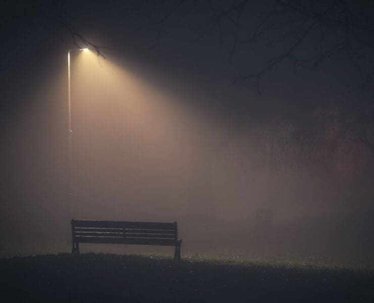 Empty bench under a streetlight in thick fog, symbolising a missing person case with no leads or clear evidence.