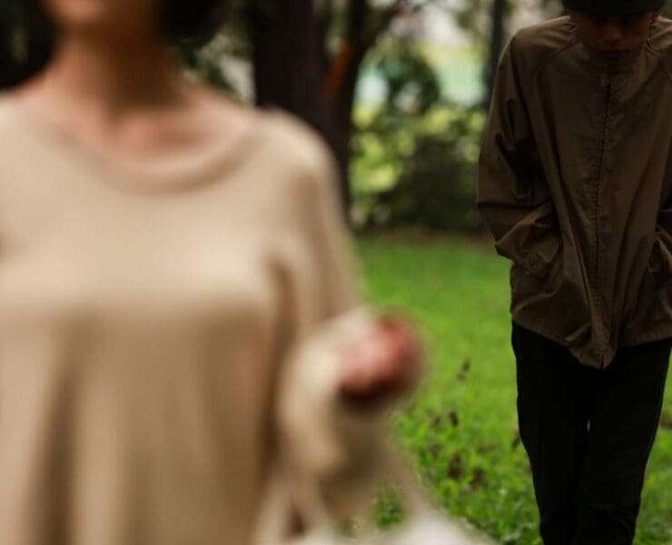 A person walking behind another in a park, creating a tense, suspenseful atmosphere used as artwork for the cinematic track The Watcher.