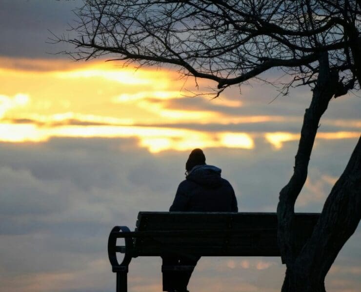 person sitting alone on a bench at sunset, reflective documentary storytelling scene with calm atmosphere