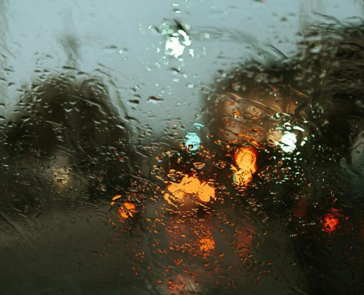 Rain-covered train window with blurred city lights at night, creating a calm and reflective urban atmosphere
