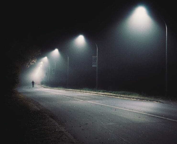 Empty road at night under streetlights with a lone figure, dark and atmospheric crime title sequence mood